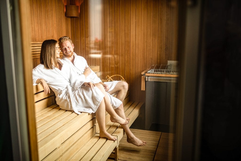 Entspannte Paare in Sauna mit Bademänteln, genießen wellness und Entspannung im Belsers Hotel. Perfekte Kulisse für Erholung und Spa-Erlebnisse in einer warmen Holzsauna.