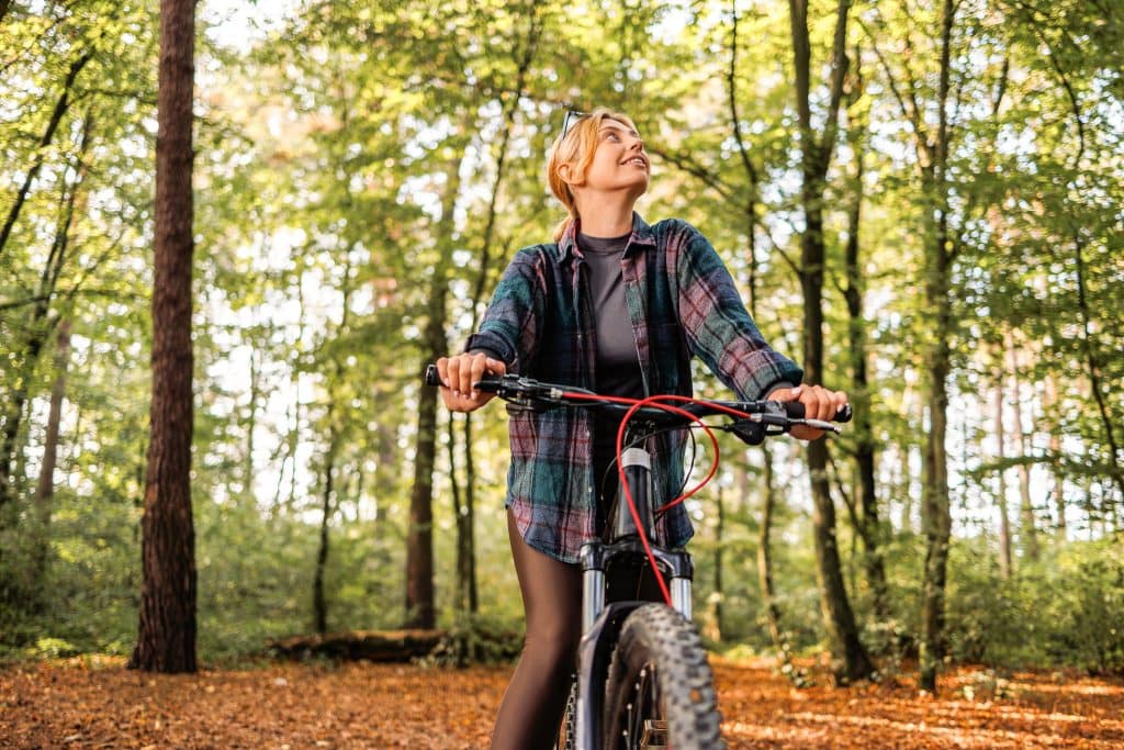 Radfahrerin in einem Herbstwald, Natur und Freizeit, Outdoor-Aktivitäten, Rad Touren, grüne Blätter, entspannter Ausflug, Damenrad, Waldspaziergang, Mountainbiking, Natur erleben.