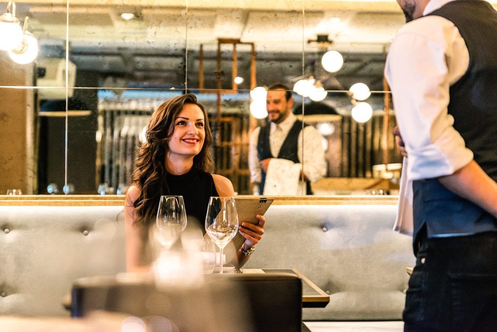 Elegante Frau im Restaurant bei Belsers Hotel, genießt feines Essen und Wein in stilvollem Ambiente, perfekte Atmosphäre für besondere Anlässe.