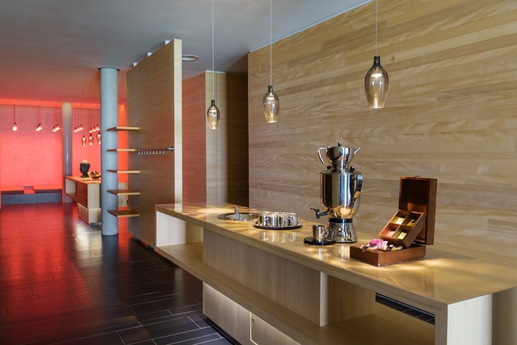 Warmer Loungetresen mit Kaffee- und Teeservice, modernes Design, Edelstahl-Kaffeemaschine, Holz-Wandverkleidung, gemütliche Atmosphäre im Belsers Hotel, ideal für entspannte Aufenthalte.