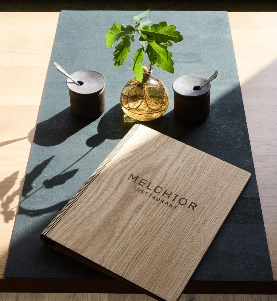 Elegante Menükarte von Belsers Hotel auf dunklem Tisch mit Kerzen und Vase, stilvolle Inneneinrichtung, ideal für einen gehobenen Aufenthalt in der Unterkunft.