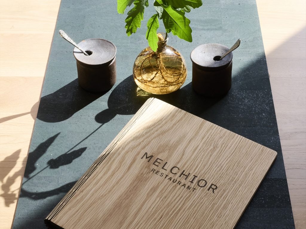 Elegante Tischdekoration im Melchior Restaurant mit Kerzen, Blumentopf und Holzmenü, ideal für ein gemütliches Essen in Belsers Hotel.