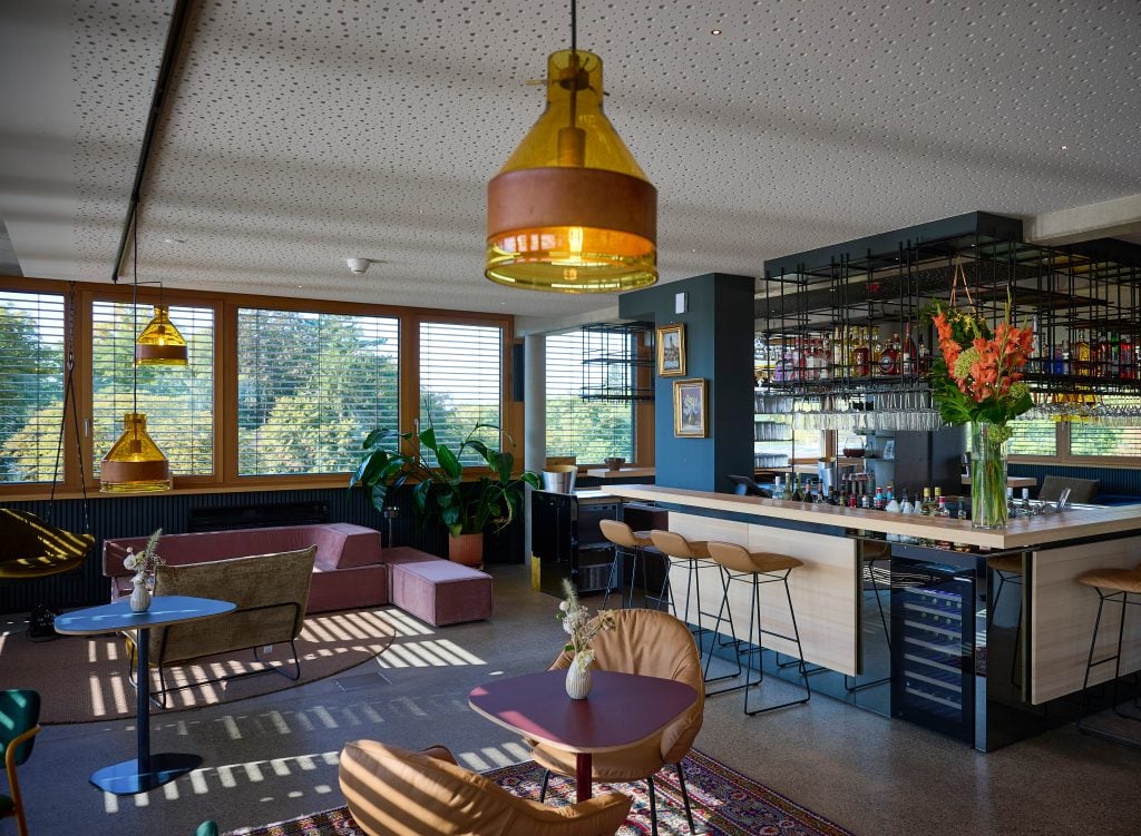Moderne Hotel-Lounge im Belsers Hotel in Nürtingen mit stilvoller Einrichtung, Barbereich und Blick auf die Natur durch große Fenster.